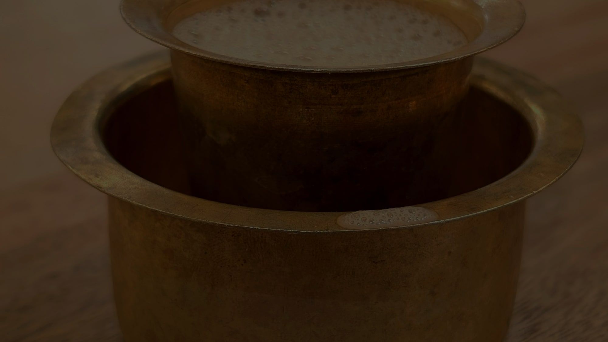 A brass davara and tumbler set, the coffee still frothing at the rim.