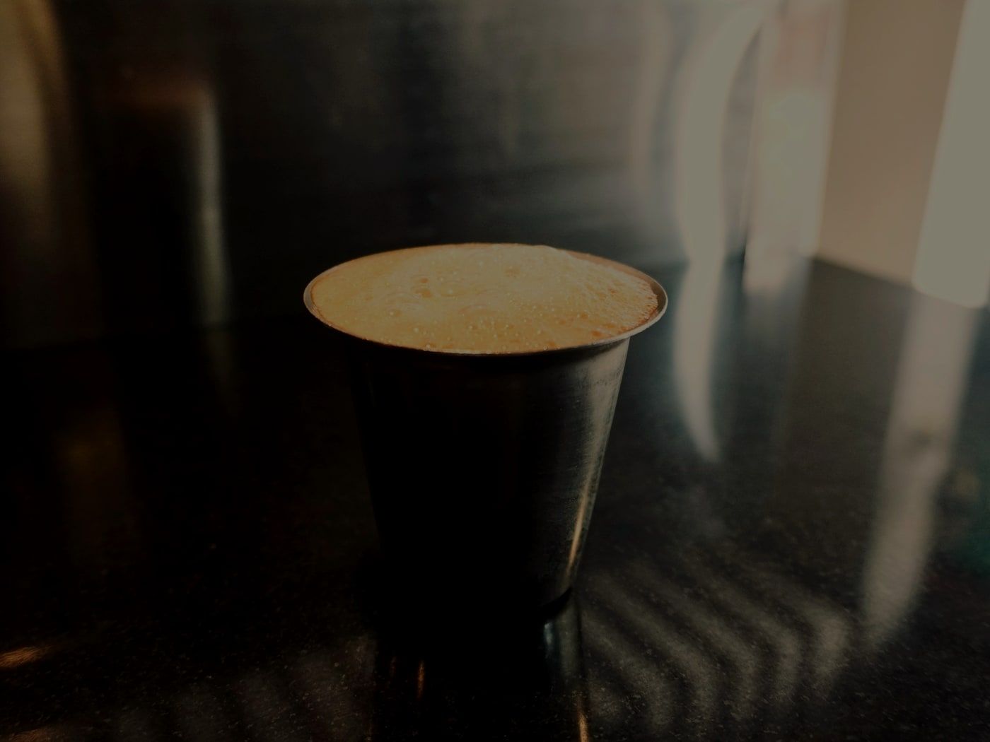 A steel tumbler of filter coffee on the counter, the froth still standing.